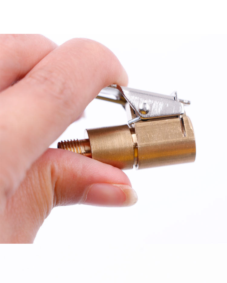 A hand holds a brass tire inflator quick-connect adapter with a clip-on lock mechanism.