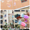 A hand is using a pink and blue automatic bubble gun to shoot bubbles onto a building.