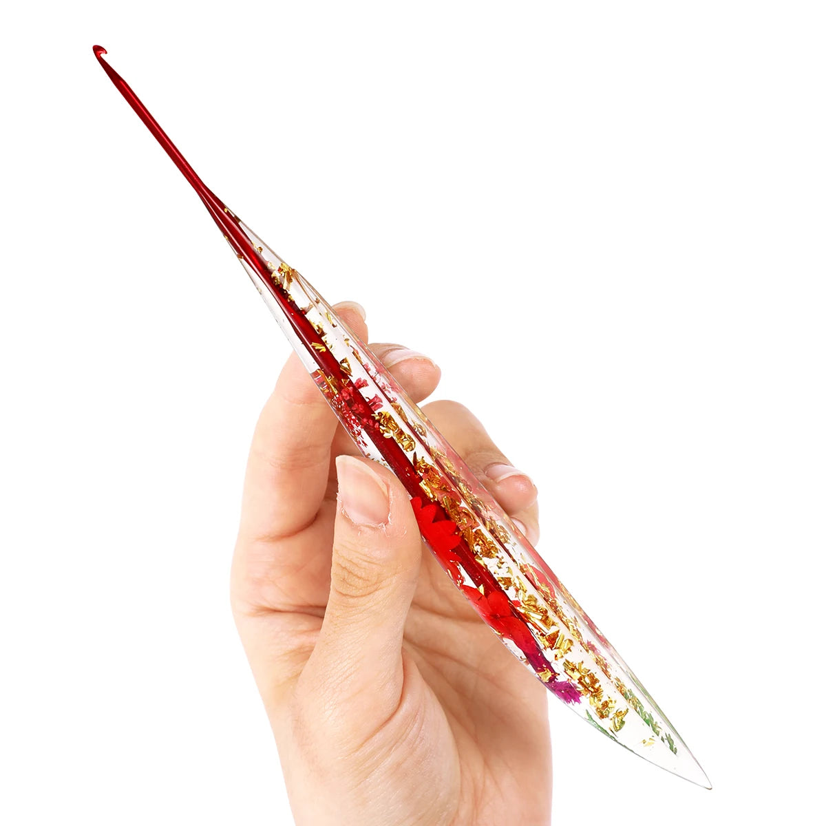 A hand holds a clear epoxy resin floral-patterned crochet hook set, showing the intricate red and gold designs.