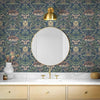 A bathroom vanity featuring blue vintage damask floral wallpaper, a gold mirror, and light wood cabinetry.