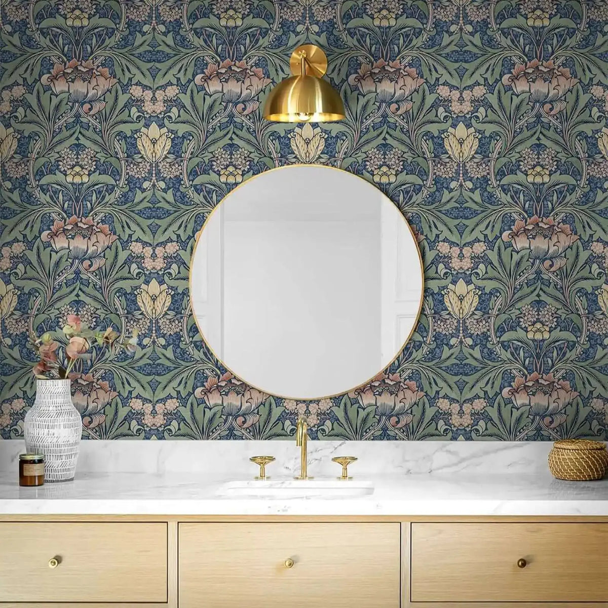 A bathroom vanity featuring blue vintage damask floral wallpaper, a gold mirror, and light wood cabinetry.