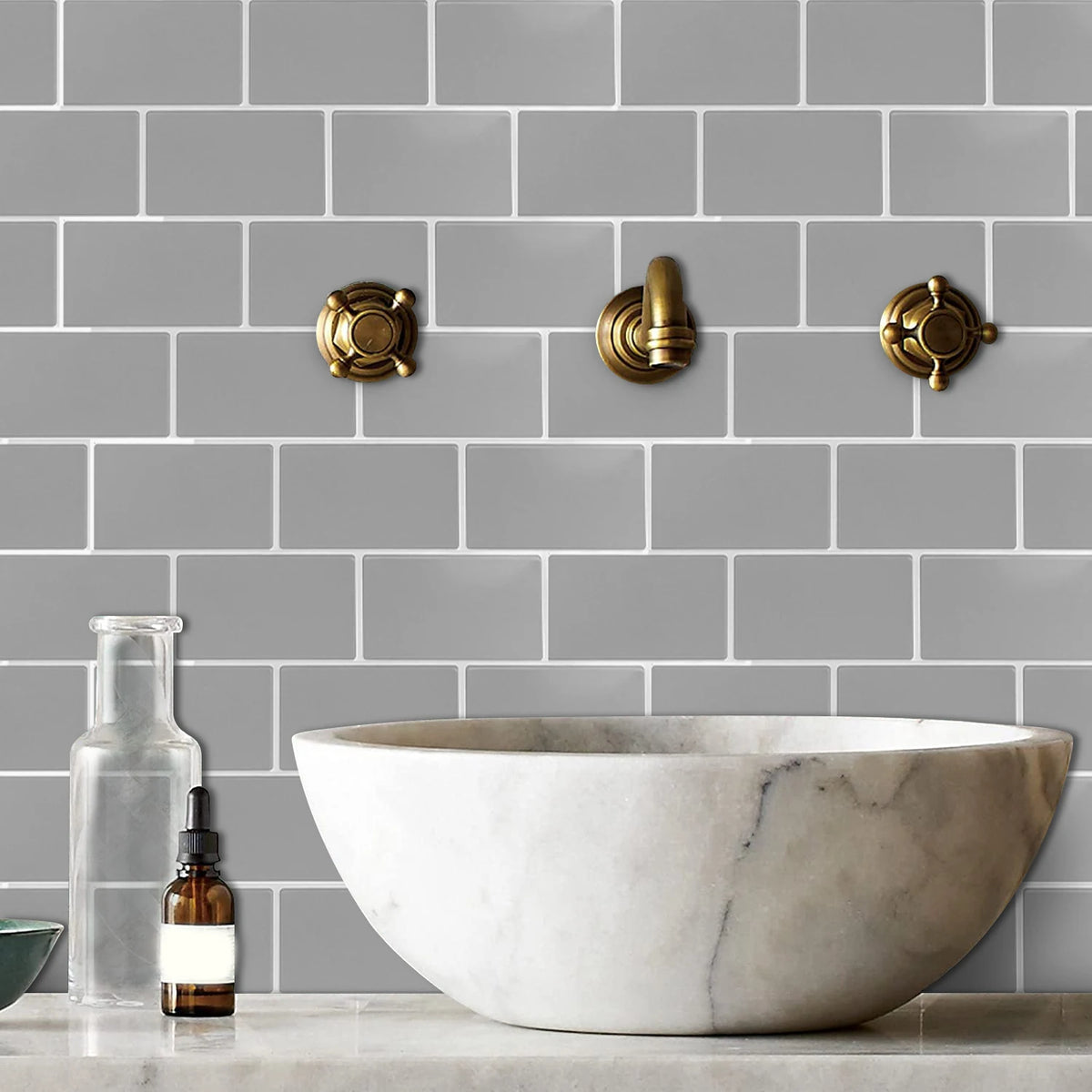 A white marble bowl sits on a countertop against a gray subway tile backsplash with brass hardware.