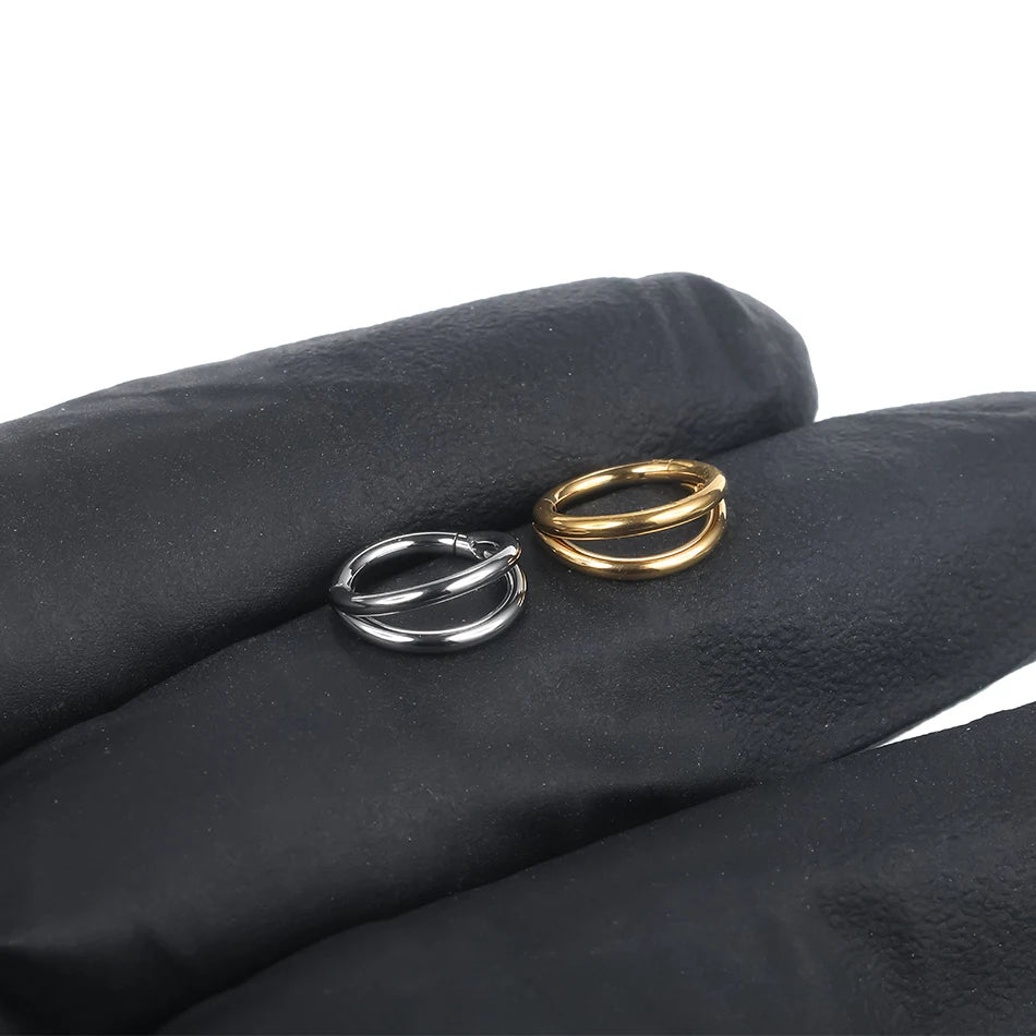 Two gold and silver titanium double hoop nose rings displayed on a black glove.