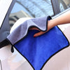 A hand is holding a blue microfiber car drying towel with a gray trim, positioned near a car window.