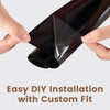 A hand is applying a roll of dark tinted car window film to a glass surface for DIY installation.