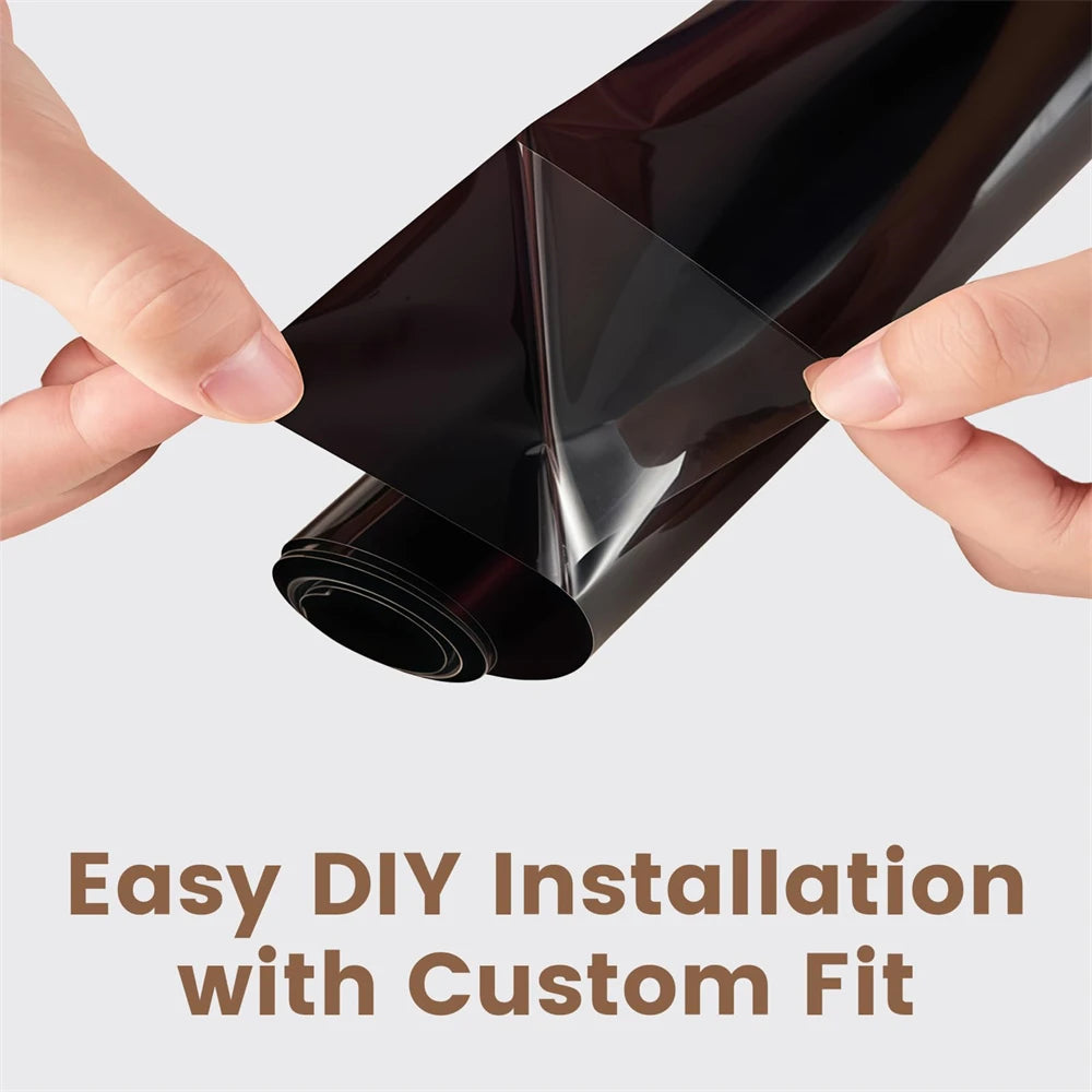 A hand is applying a roll of dark tinted car window film to a glass surface for DIY installation.
