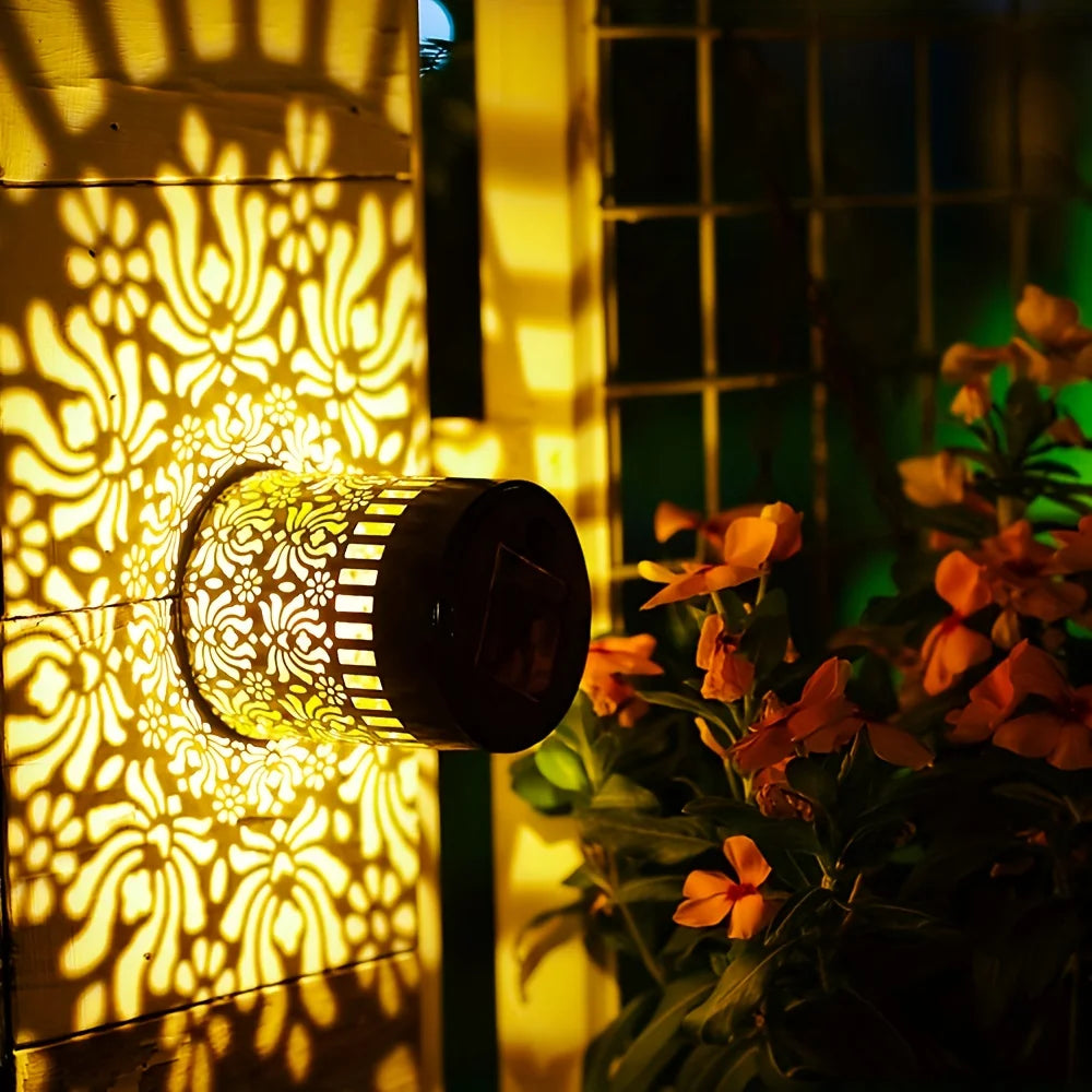 A solar peony wall light casts intricate floral shadows on a textured wall next to green foliage.