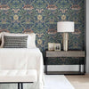 A bedroom featuring a headboard and nightstand decorated with blue vintage damask floral wallpaper.