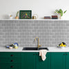 A kitchen countertop with a black sink, green cabinets, and a gray subway tile backsplash.