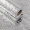 Roll of self-adhesive aluminum foil kitchen backsplash protector lying on a reflective surface.