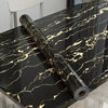 A roll of black and gold marble peel-and-stick wallpaper film displayed on a dark table surface.
