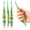 A hand holds a set of epoxy resin floral-patterned crochet hooks, showing the green and teal designs.