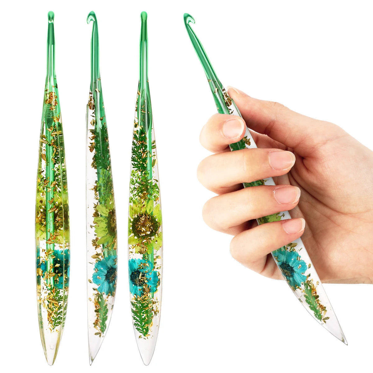 A hand holds a set of epoxy resin floral-patterned crochet hooks, showing the green and teal designs.