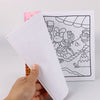 A hand holds an open coloring book page featuring a line drawing of cartoon animals for adults and teens.