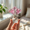 Eine Hand hält eine Kristall-Rose-Figur mit einer Glasvase gefüllt mit rosa Kristallrosen.