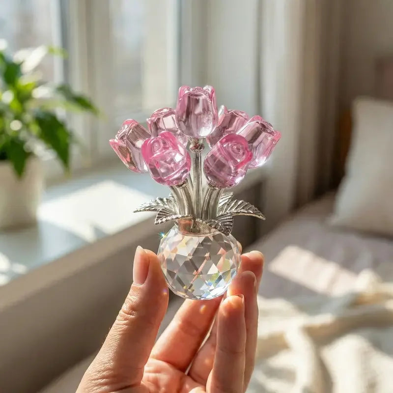 Eine Hand hält eine Kristall-Rose-Figur mit einer Glasvase gefüllt mit rosa Kristallrosen.