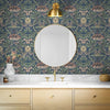A bathroom vanity featuring blue vintage damask floral wallpaper, a gold mirror, and light marble countertop.