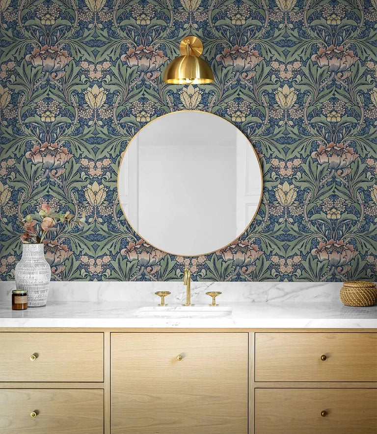 A bathroom vanity featuring blue vintage damask floral wallpaper, a gold mirror, and light marble countertop.