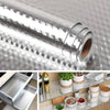 Roll of self-adhesive aluminum foil kitchen wall stickers shown next to a stainless steel storage rack.
