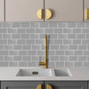 A kitchen countertop with a white sink and faucet set against a gray subway tile backsplash and light gray cabinetry.