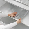 A hand is placing self-adhesive aluminum foil kitchen wall stickers onto a smooth, light gray cabinet surface.