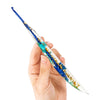 A hand holds a slender epoxy resin crochet hook with a floral pattern, showing its clear and blue coloration.