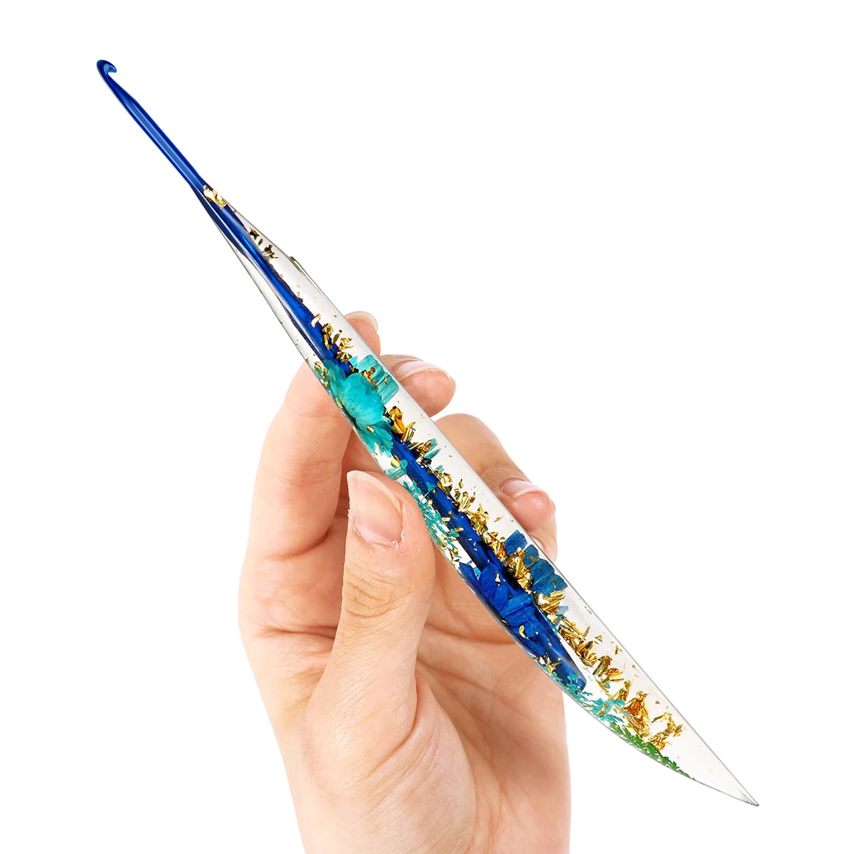 A hand holds a slender epoxy resin crochet hook with a floral pattern, showing its clear and blue coloration.