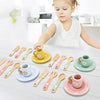 A set of wooden cookie play food and baking accessories with various sized spoons and cups on a white surface.