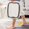 A person holds a white collapsible foot spa bucket with massage nodules, resting on a light-colored rug.