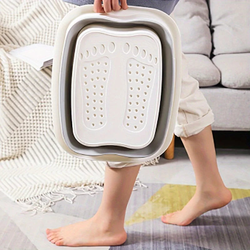 A person holds a white collapsible foot spa bucket with massage nodules, resting on a light-colored rug.