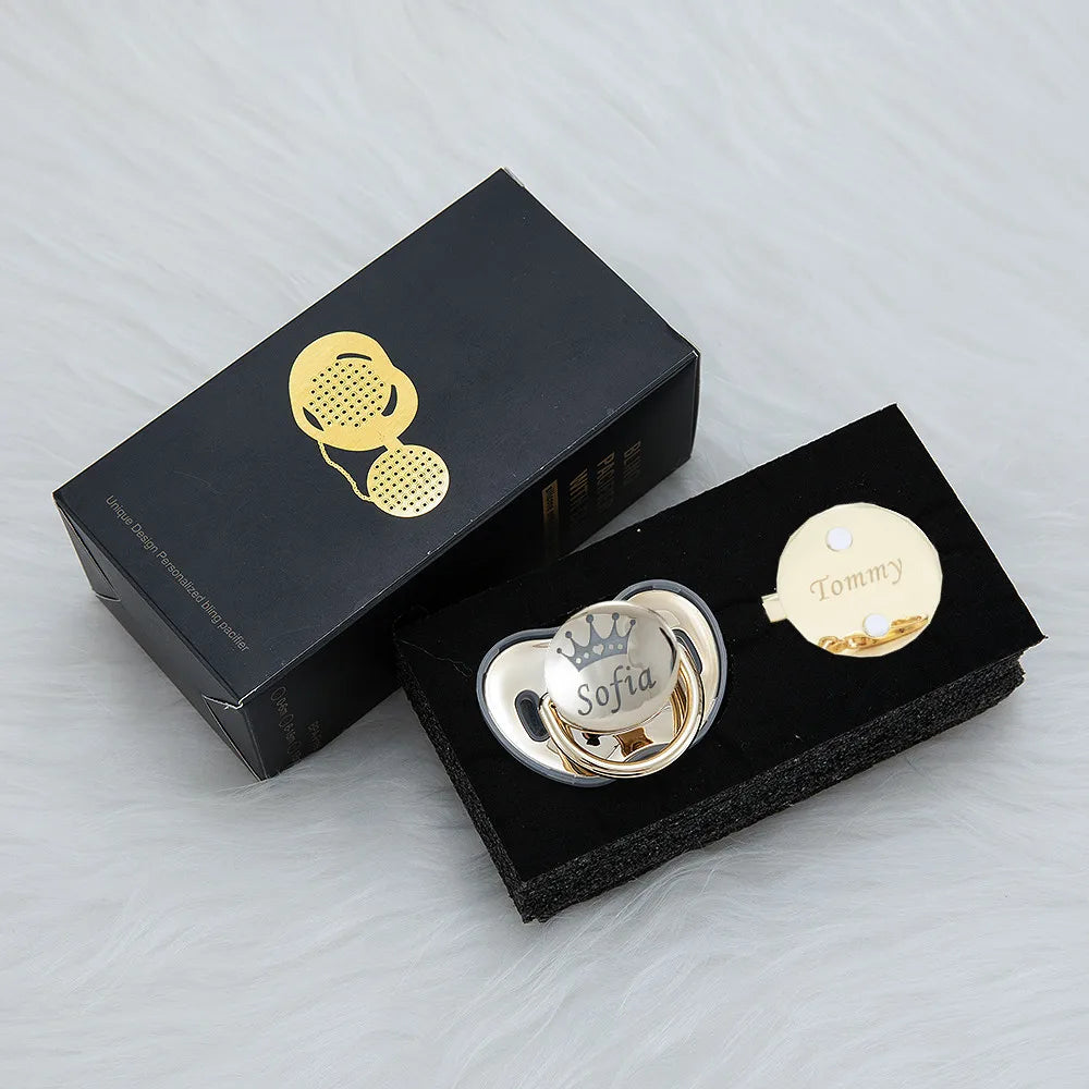 A black box containing a personalized rhinestone pacifier and clip set with a gold-toned charm.
