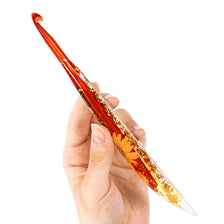 A hand holds an orange epoxy resin floral-patterned crochet hook set, showing the detailed design and color.