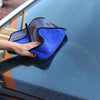 A hand is wiping a car window with a blue and gray microfiber drying towel.