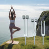 A woman stands on a grassy cliff overlooking the sea, holding tuning forks for sound therapy and meditation.