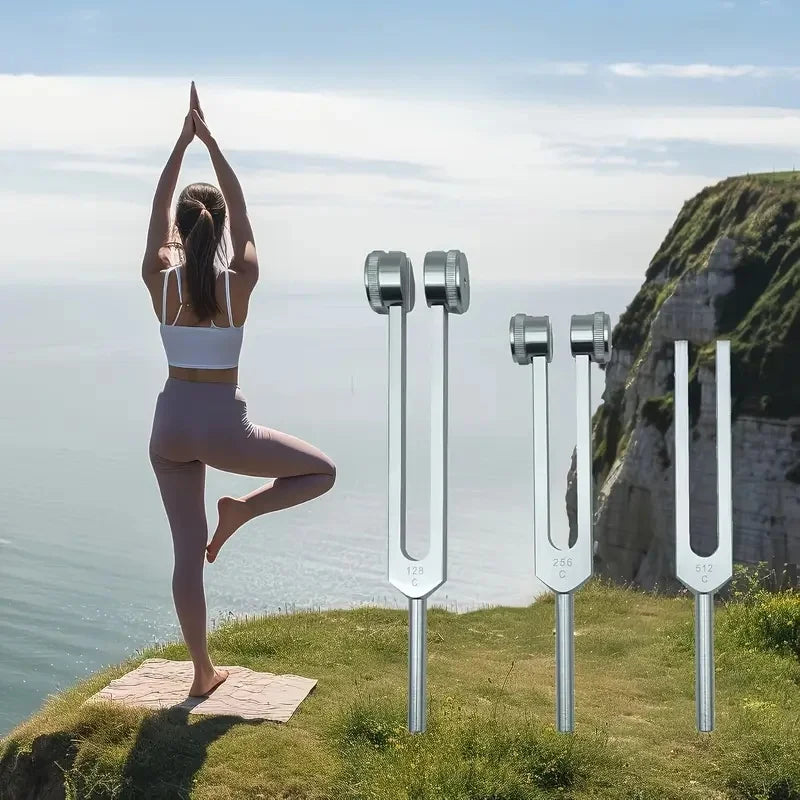 A woman stands on a grassy cliff overlooking the sea, holding tuning forks for sound therapy and meditation.