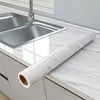 Roll of pearl finish waterproof self-adhesive wallpaper placed on a kitchen countertop next to a stainless steel sink.