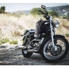 A black motorcycle is parked on a dirt road with a black waterproof cover draped over the seat.