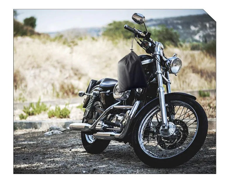 A black motorcycle is parked on a dirt road with a black waterproof cover draped over the seat.