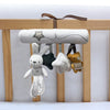 A soft plush bunny rattle toy hanging from a wooden bar, featuring a large rolled shape and several small stuffed animals.