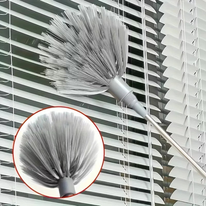 A silver adjustable spider web ceiling cleaner with a microfiber head hanging against a slatted window.