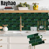 A kitchen backsplash featuring dark green subway tiles and a gold faucet, with white countertops and cabinetry.