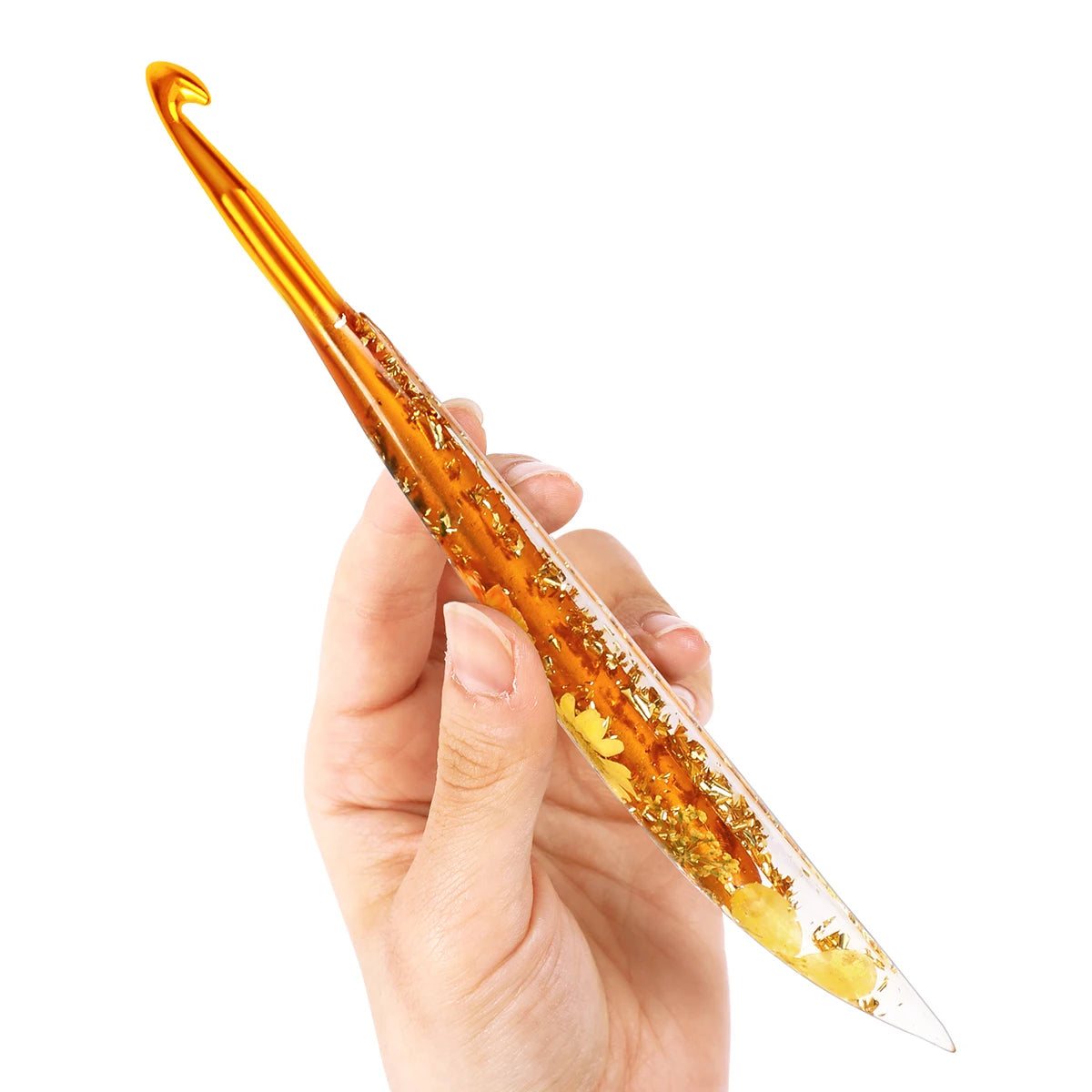 A hand holds an epoxy resin floral-patterned crochet hook set, showing the golden-amber color and pointed tips.