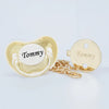 Gold-toned pacifier and clip set with a heart-shaped charm engraved with the name Tommy