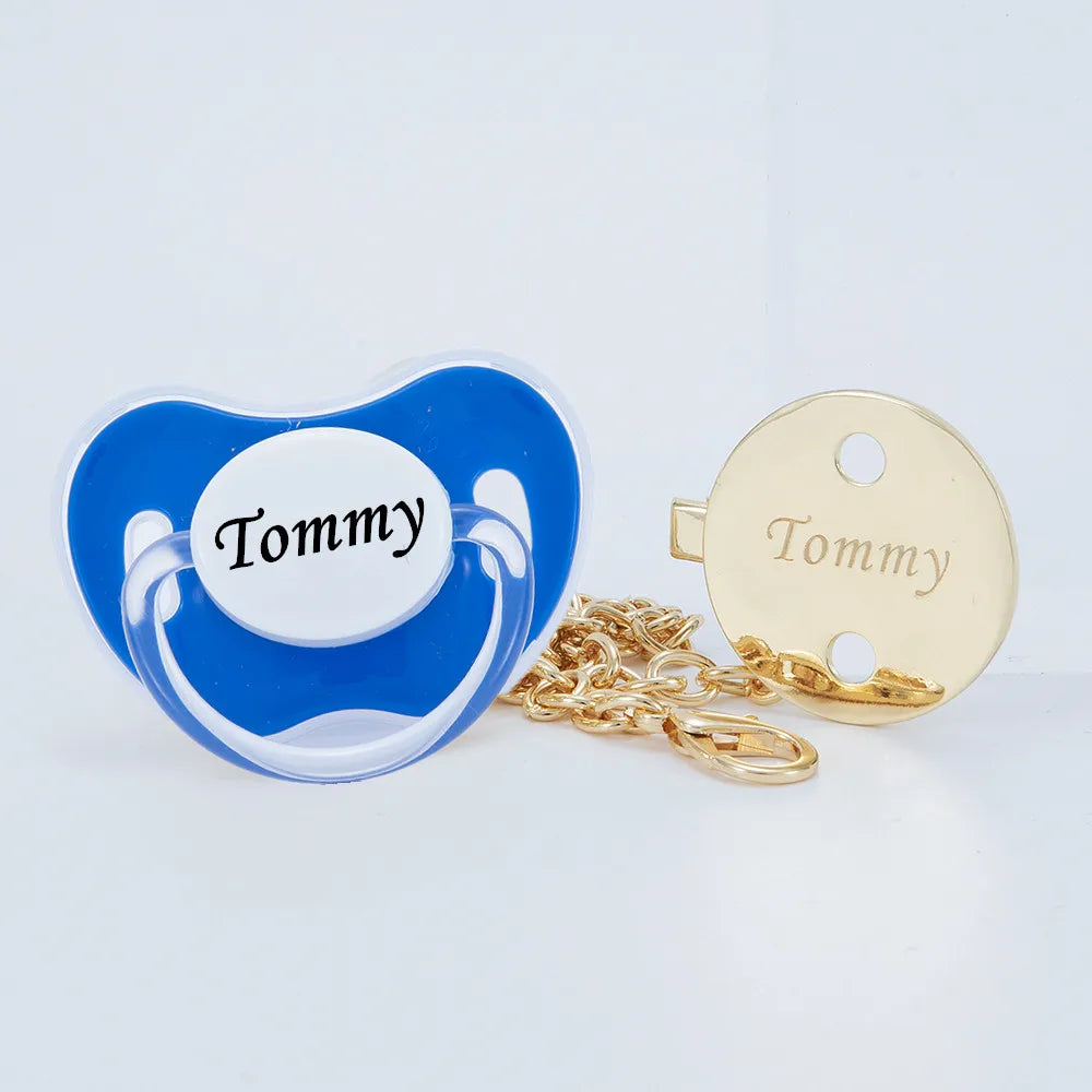 A clear blue silicone pacifier with the name Tommy and a gold-colored clip set.