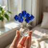Eine Hand hält eine Kristall-Rosenfigur in einer Glasvase mit blauen Kristallrosen.