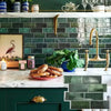A kitchen backsplash featuring dark green subway tiles, a marble countertop with baked goods, and a gold faucet.