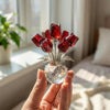 Eine Hand hält eine Kristall-Rose-Figur mit Glasvase, tiefroten Rosen und silbernen Akzenten.
