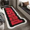 Una alfombra de bienvenida decorativa roja y negra con letras llamativas yace sobre un suelo de madera.