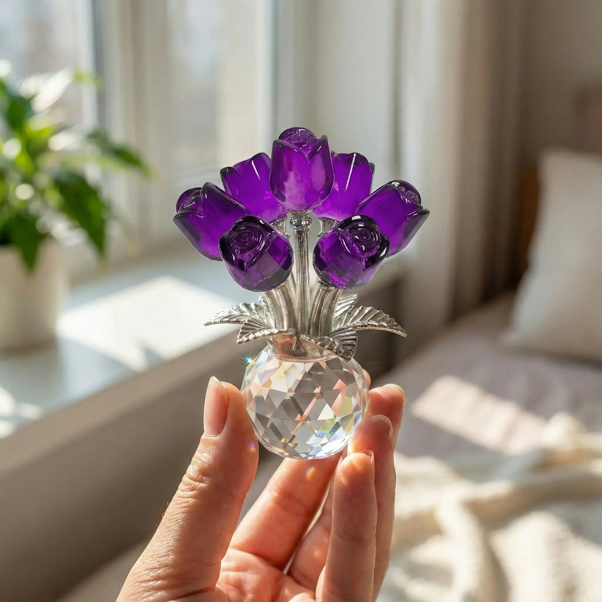 Eine Hand hält eine Kristall-Rosenblütenfigur mit einer Glasvase, die tiefe violette Blumen und silberne Akzente zeigt.