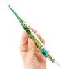A hand holds a set of epoxy resin floral-patterned crochet hooks with green handles and clear bodies.